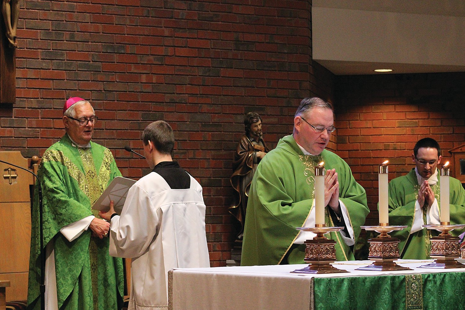 Father Michael McMahon professes his oath at the altar as Bishop Thomas J. Tobin installs him as the new pastor of St. Philip’s Church, with Assistant Pastor  Father Phillip Dufour, at right.